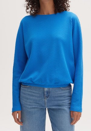 Sweatshirt bleu texturé avec un col rond et des manches longues, présentant une coupe décontractée et un léger élastique à l'ourlet, associé à un jean.