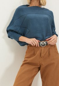 Blauwe gebreide oversized trui met textuurpatroon, gedragen met hoge, bruine corduroy broek en een zwarte riem met zilverkleurige accenten.