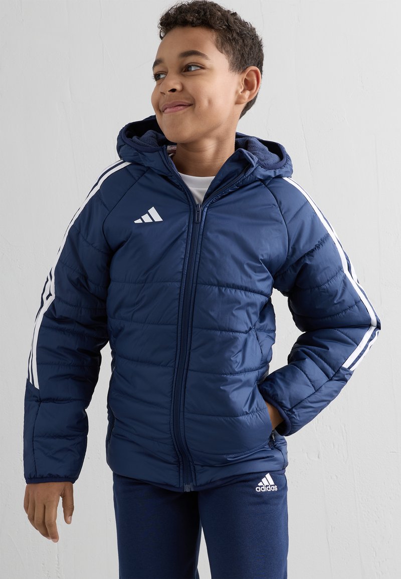 Granatowa kurtka puchowa z białymi paskami na rękawach i logo Adidas, z kapturem, zamkiem błyskawicznym i pikowaną teksturą.