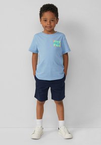 Lichtblauwe T-shirt met korte mouwen en de grafische tekst "GET FUN", gecombineerd met marineblauwe shorts. Witte sneakers en enkelsokken maken de outfit compleet.