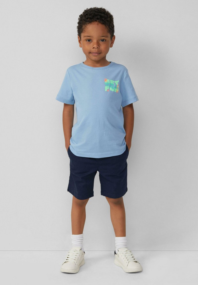 Lichtblauwe T-shirt met korte mouwen en de grafische tekst "GET FUN", gecombineerd met marineblauwe shorts. Witte sneakers en enkelsokken maken de outfit compleet.