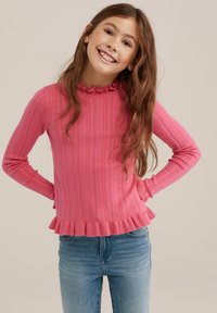 Rožinė megzta palaidinė su rausvu raštu, su raukšlėta apykakle ir peplum siluetu, derinama su mėlynomis džinsinėmis kelnėmis.