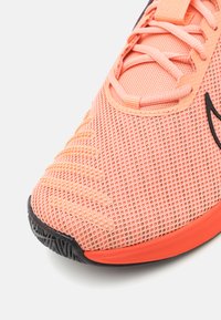 Chaussure de sport lég�ère en mesh orange avec surface texturée et semelle en caoutchouc noire. Elle possède des lacets plats et un embout renforcé.