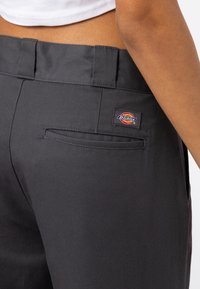 Tmavě šedé kalhoty vyrobené z odolné tkaniny, které mají zadní kapsu s malým vícebarevným logem Dickies a plochý design pasu.