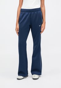 Ναυτικό μπλε αθλητικά παντελόνια με χαλαρή γραμμή, ελαστική μέση και λευκές ρίγες στο πλάι, φτιαγμένα από μαλακό, ελαστικό υλικό. Ο λογότυπος της Nike είναι ορατός.