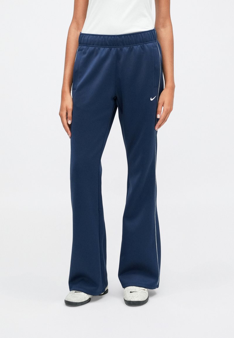 Pantaloni sportivi blu navy con vestibilità rilassata, vita elastica e strisce laterali bianche, realizzati in materiale morbido e elasticizzato. Logo Nike visibile.