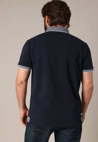Polo shirt navy avec un col et des finitions de manche contrastants en bleu clair, fabriqué en coton, présentant une coupe droite et des fentes latérales.