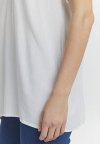 Hvid, letvægts bluse med en struktureret overflade, der har en løs pasform, rundet kant og som er parret med mørkeblå denim.