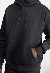 Černá mikina z bavlněné směsi s klokaní kapsou, nastavitelnými šňůrkami a texturovanými bočními panely. Diskrétní logo na hrudi.