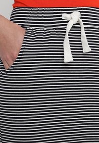 Randigt svart och vitt tyg med elastisk midja och vit dragsko. Har sidofickor och en slät textur.