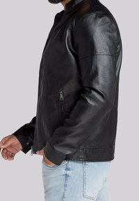 Giubbotto in pelle nera con zip frontale, tasche laterali e una texture liscia. Presenta un colletto rialzato e un design aderente.