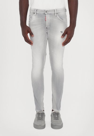 Šedé džíny skinny s mírným vyblednutím, poškozenými detaily a zapínáním na knoflík, spárované se šedými semišovými teniskami.