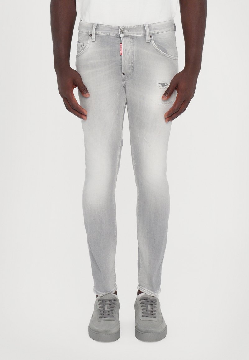 Jean skinny en denim gris avec un léger délavage, des détails usés et une fermeture à bouton, assorti à des baskets en daim gris.