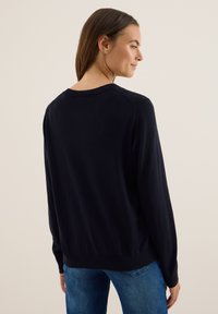 Marineblauwe trui met lange mouwen, geribbelde ronde hals en zoom, zachte textuur en een relaxed fit. Achteraanzicht toont naaddetails.