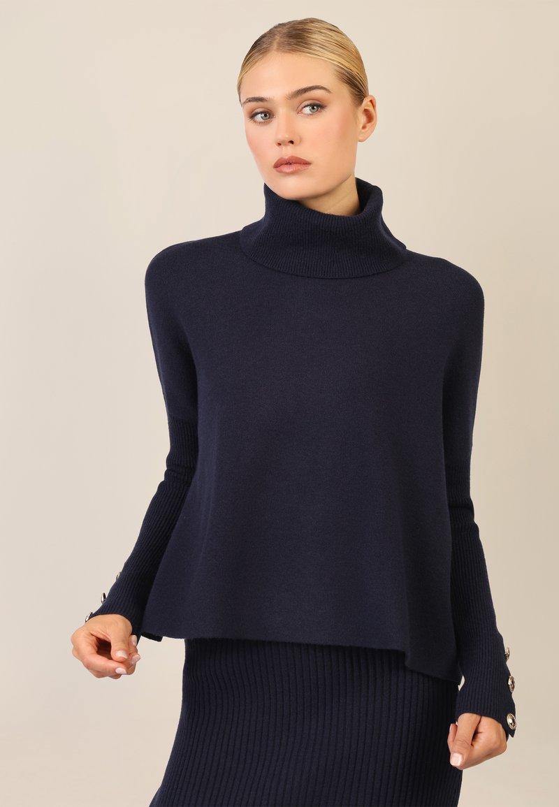 Marineblauer Rollkragenpullover aus weichem Strick, mit gerippten Bündchen und Knopfdetails sowie einer lockeren Passform, kombiniert mit einem passenden gerippten Unterteil.