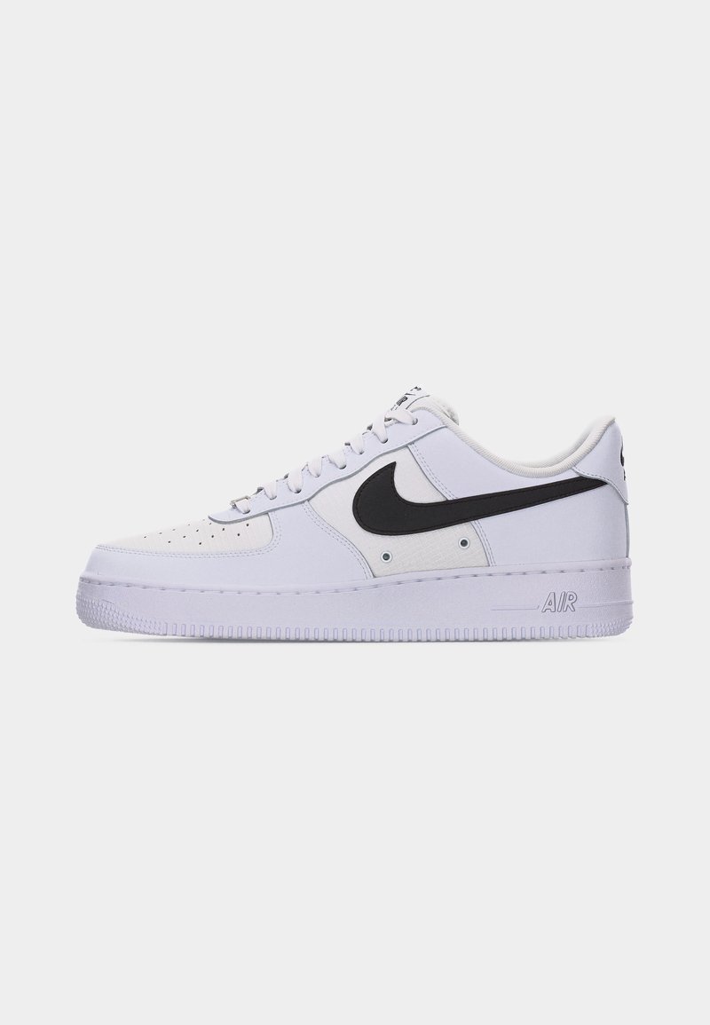 Baskets Nike Air Force 1 blanches avec logo swoosh noir sur le côté, lacets blancs et orteil perforé sur un fond uni.
