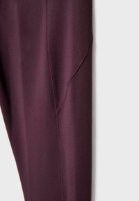 Legginsy w głębokim burgundzie, wykonane z gładkiego, elastycznego materiału z konturowym przeszyciem wzdłuż uda.