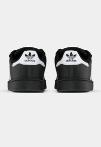 Svart-hvite Adidas-sneakers med glatt syntetisk overdel, avrundet tå, polstret krage og signatur trefoil-logo på hælen.