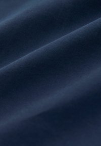 Gros plan sur un tissu bleu foncé lisse avec une texture diagonale fine à côtes et des plis doux.