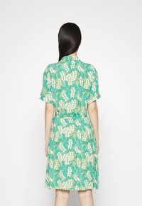 Kurzes Kleid mit kurzen Ärmeln aus einem grünen Stoff, der ein florales Muster mit blauen Blättern und weißen Blüten zeigt, mit Taillenzug und lässiger Passform.