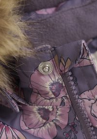 Lilla blomstret jakke med detaljer, der har en sølv trykknap, tekstureret stof og falsk pelskant langs kraven.