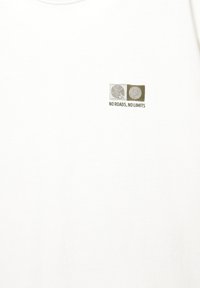 Hvid bomulds-t-shirt med et lille grafisk design med to cirkulære motiver og teksten "NO ROADS, NO LIMITS" i grøn.