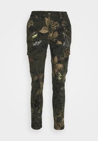 Pantalon camouflage avec un motif floral vert foncé et marron, doté de poches zippées et d'accents de paillettes pour plus de détails.
