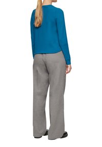 Turquoise gebreide trui met lange mouwen, gecombineerd met grauwe wijde broek. De outfit heeft een eenvoudig, gestructureerd ontwerp en een zachte textuur.
