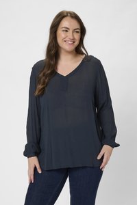 Mörkblå långärmad blus med V-ringning, tillverkad av ett lätt, texturerat tyg och med rynkade manschetter. Matchas med mörk denim.