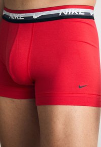 Rote Baumwoll-Boxershorts mit einem schwarz, grau und weißen gestreiften Bund, der das "NIKE"-Logo trägt, eng anliegend und mit glatter Textur.