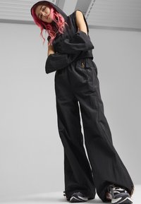 Ensemble noir à capuche sans manches avec un pantalon large. Comprend des poches à fermeture éclair et un tissu texturé pour flexibilité et confort.