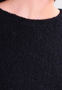 Svart texturerad tyg med en mjuk, ludden yta. Har en rund halsringning och en enkel, odekorerad design.