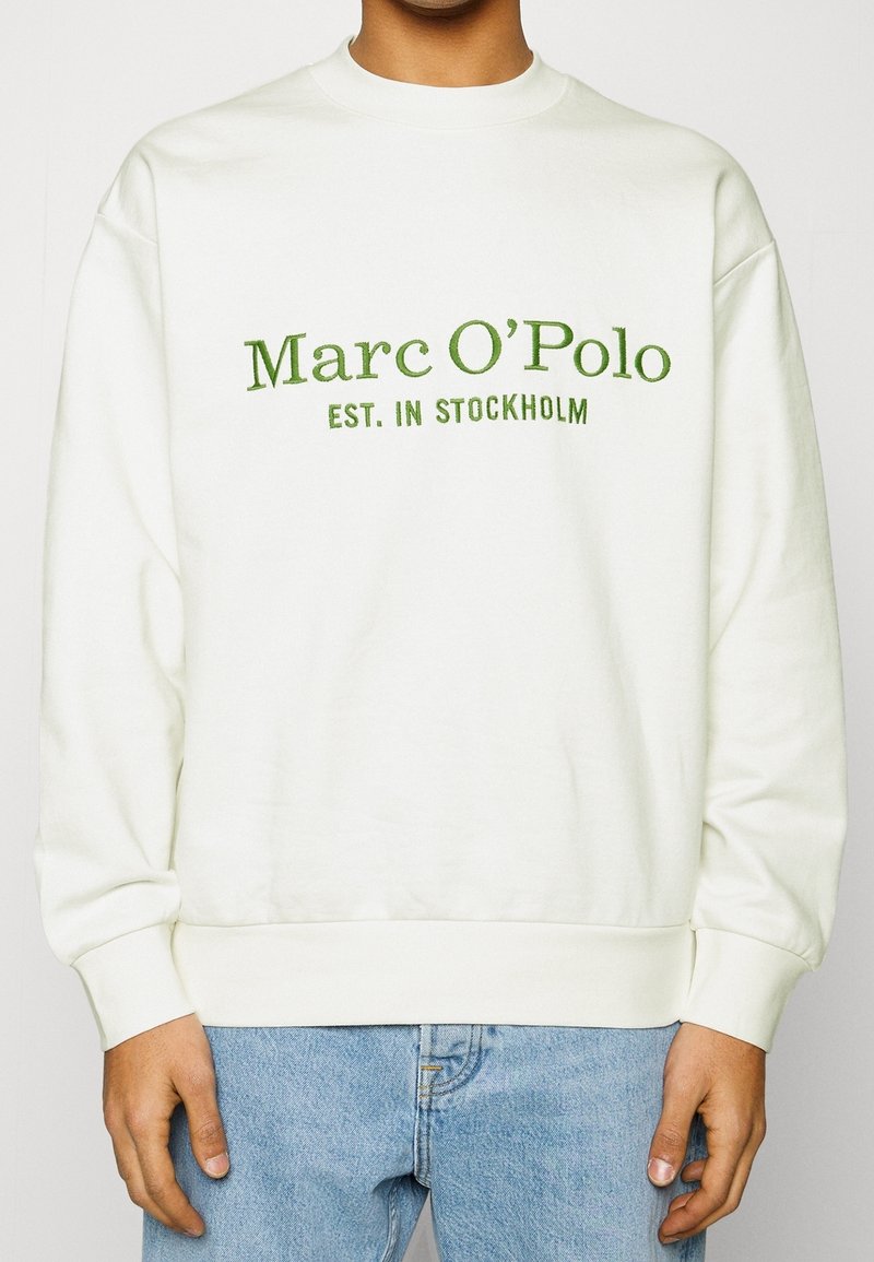 Sweat-shirt couleur crème avec texte brodé en vert indiquant "Marc O'Polo EST. IN STOCKHOLM", avec un col rond et des poignets côtelés.
