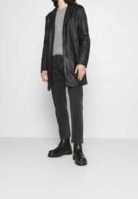 Manteau en cuir noir avec un col à revers, associé à un t-shirt gris et un jean foncé. Bottines noires à semelles épaisses. Texture lisse dans l'ensemble.