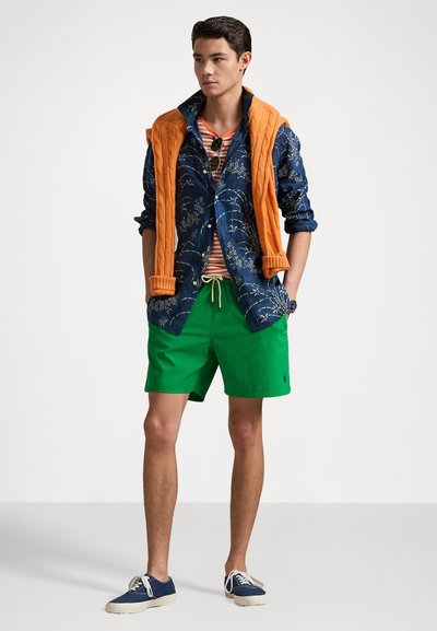 Cămașă cu nasturi, de culoare bleumarin, cu un model floral, pulover portocaliu drapat, tricou cu dungi, pantaloni scurți verzi, pantofi casual bleumarin cu tălpi albe.
