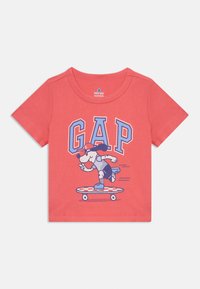 Koralo spalvos trumpomis rankovėmis marškinėliai, pagaminti iš medvilnės, su grafika, vaizduojančia šunį, važiuojantį riedlente, ir „GAP“ užrašu mėlyna ir balta spalvomis.