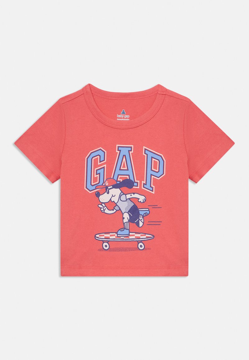 Kora īsām piedurknēm T-krekls, izgatavots no kokvilnas, ar grafiku, kurā redzams suns uz skeitborda, un tekstu "GAP" zilā un baltā krāsā.