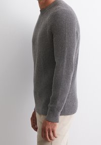 Šedý žebrovaný pletený svetr s dlouhými rukávy a kulatým výstřihem, s jemným vzorem a přiléhavým lemem. Stylizován s lehkými kalhotami.