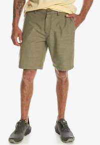 Olivenfarvede shorts lavet af struktureret stof, med frontlukning med knap, bæltesløjfer og skrå lommer på hver side.