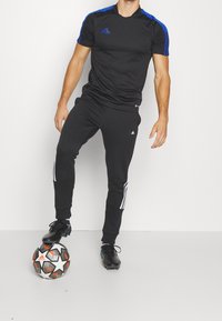 Camiseta atlética negra con acentos azules, joggers negros con rayas blancas a los lados, combinados con tacos de fútbol negros y un balón de fútbol estampado.