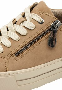 Tan suede sneaker with cream laces, featuring a side zipper, textured stitching, and a thick cream rubber sole.