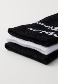 Montón de calcetines que incluye dos calcetines negros con patrones blancos y un calcetín blanco, hecho de algodón acanalado, con una textura suave.