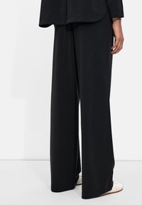 Black wide-leg pants made of smooth fabric, featuring a loose fit that tapers slightly at the hem; paired with light-colored shoes.