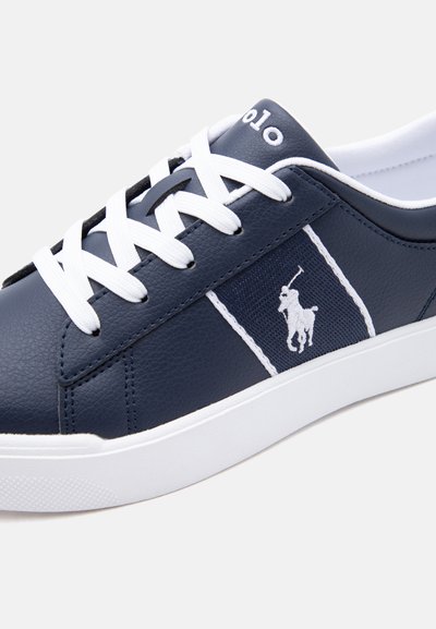 Σκούρο μπλε αθλητικό παπούτσι με λευκά κορδόνια, λευκή σόλα και κεντημένο λογότυπο παίκτη πόλο στην πλαϊνή επιφάνεια.
