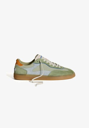 Zapatillas de ante verdes y azules con suela de goma, que presentan cordones blancos, acentos naranjas en el talón y detalles de costura.