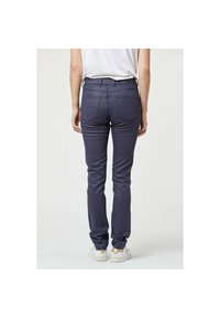 Marineblauwe slim-fit broek met een gladde textuur, twee achterzakken en een middelhoge taille, gecombineerd met witte sneakers.