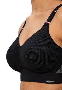 Schwarzer Sport-BH mit einem strukturierten Mesh-Design, verstellbaren Trägern und einem weißen Logo am unteren Rand. Enthält subtile geometrische Akzente.