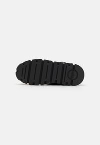 Black rubber shoe sole featuring deep grooves, circular logo, and a flat, sturdy design for enhanced traction and durability.