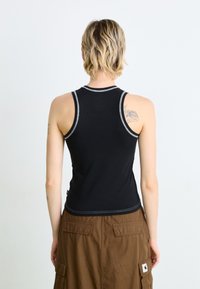 Svart ermeløs tanktop med en tettsittende design og kontrasterende hvit søm, sammen med et brunt cargo-skjørt med flere lommer.