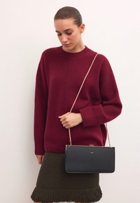 Bordo megztinis, juoda odinė rankinė su auksine grandinės dirželiu, tekstūruota žalia sijonas su šoninėmis kutais. Paprastas, elegantiškas apranga.